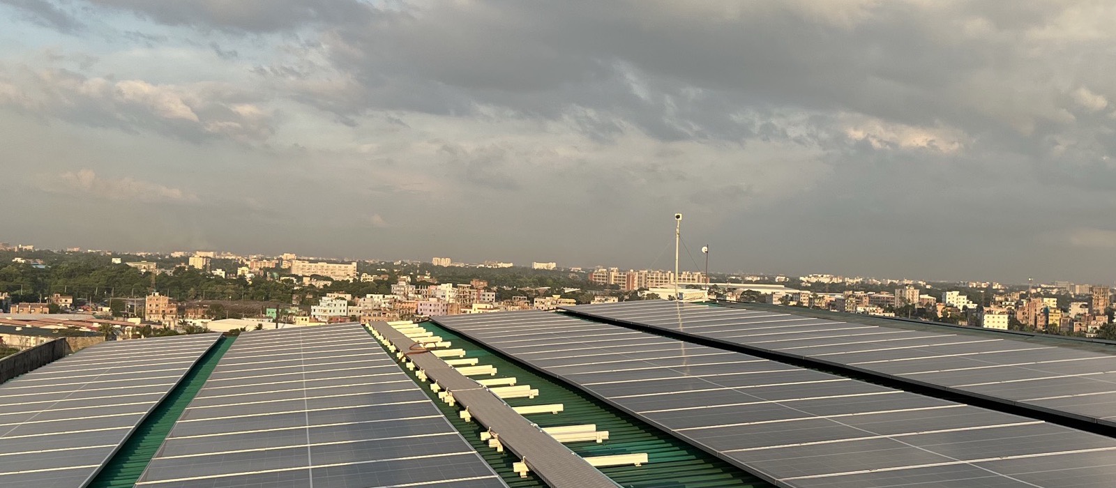 Solar panels covering a factory rooftop, with a city behind — the kind of roof a zero-investment solar plant is built on
