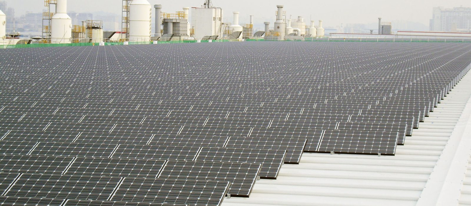 Rows of solar panels covering the metal-sheet roof of a large factory