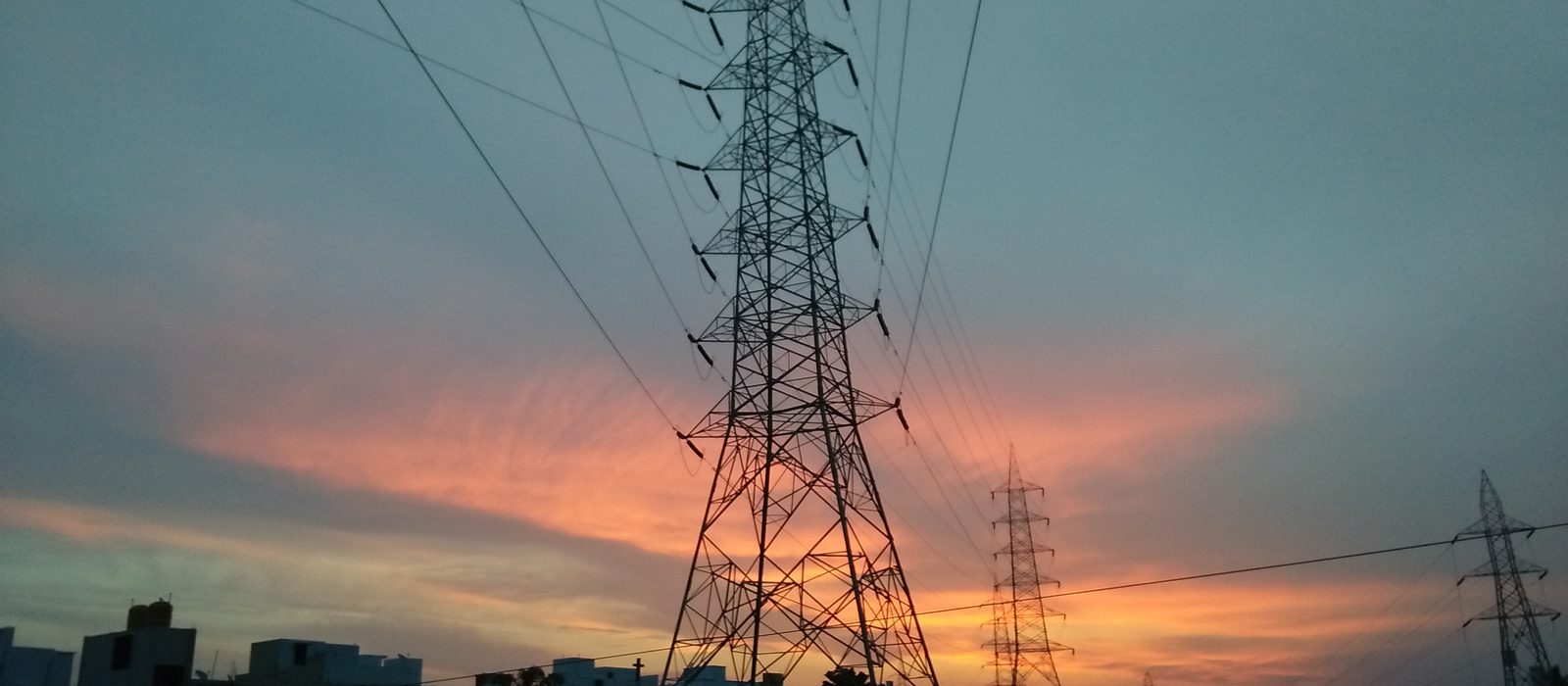 High-voltage transmission towers against an orange evening sky in Chennai